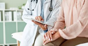  doctor pointing to a tablet next to a patient with their hands on their lap.  
