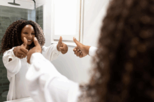 A woman smiling at herself in the mirror and giving a thumbs up.