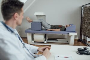 Young physician conducting a bone density scan while the patient lays on his back on the scanning table. 