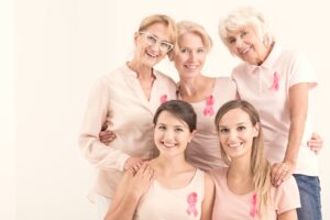 Five smiling women of various ages wearing pink ribbons. 