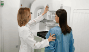 A radiologist tech adjusting the mammogram machine next to a woman who is about to get a mammogram.