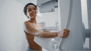 A woman standing in front of a mammography machine smiling while she has her mammogram. 