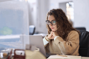 A young woman with brown hair and glasses looking at a laptop and researching imaging tests like X-rays.