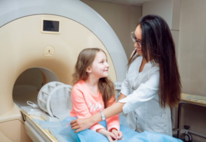 A Child Sits on the Table of an MRI Machine While a Friendly Female Tech Attends to Her