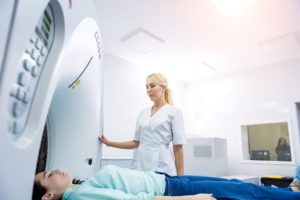 A picture of a doctor next to a CT scan machine and a patient laying down.