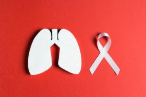 A red background with a white cutout shaped like lungs and a white ribbon for lung cancer awareness.