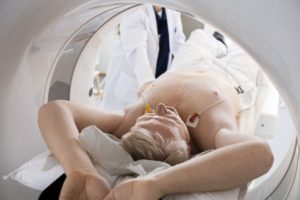 A Man with His Arms Above His Head and ECGs on His Chest is in a Machine Used for Cardiac Testing.