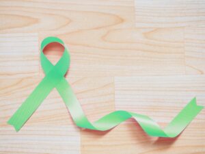 A green ribbon for Celiac Disease Awareness Month on a light wood floor. 