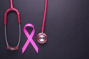 A pink stethoscope next to a pink ribbon on a dark grey background.