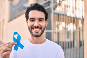 Smiling man holding a blue Prostate Cancer Awareness Month ribbon. 