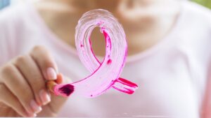 Closeup of the hand of a woman painting a pink breast cancer ribbon on a window.