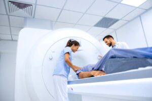 A radiologist and medical assistant smiling at a patient as they are about to enter a CT scan. 