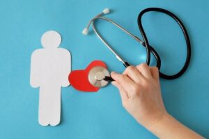 A paper cutout of a person next to a red heart with a hand holding a stethoscope over it. 