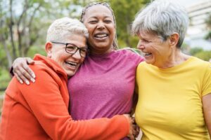 Three older women smiling, hugging, and laughing together.
