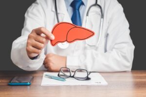 A doctor wearing a white coat at a desk holding a paper liver cutout.