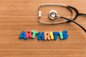 Foam children’s learning letters spell the word ARTHRITIS on a wooden surface next to a stethoscope.