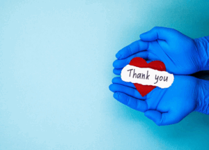 A blue background with hands in blue medical gloves to the right holding a paper heart with the words thank you. 