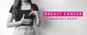 The torso of a woman in a black crop top cupping her breast and holding a pink ribbon for Breast Cancer Awareness Month.